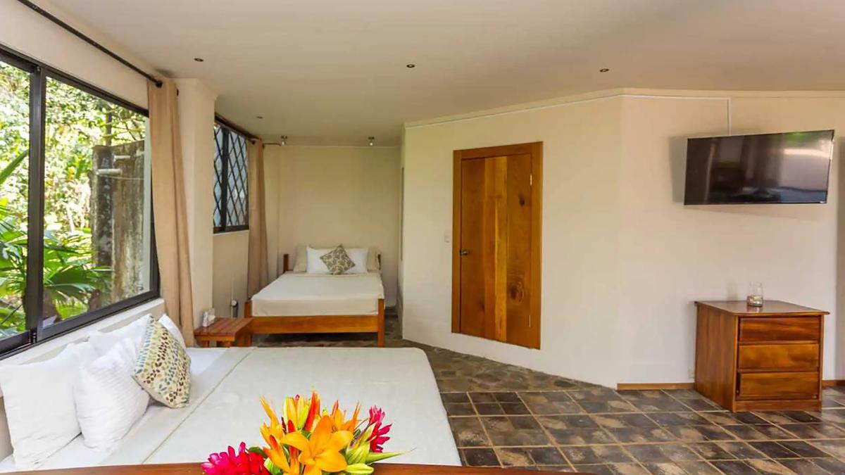 Casa Luz bedroom with two beds, wall mounted TV and tropical flowers