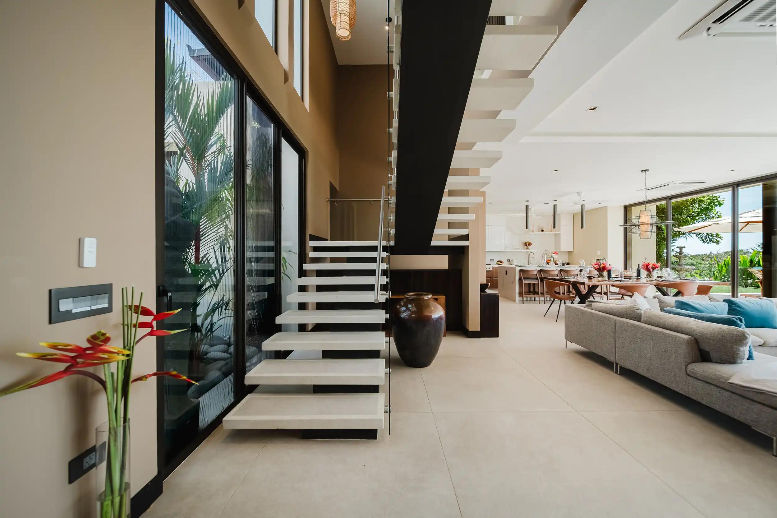 Floating staircase inside Casa Nola with glass rail, heliconia flowers, and open living area