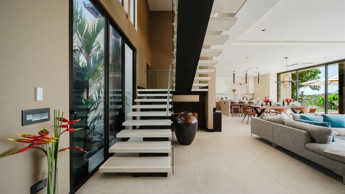 Floating staircase inside Casa Nola with glass rail, heliconia flowers, and open living area