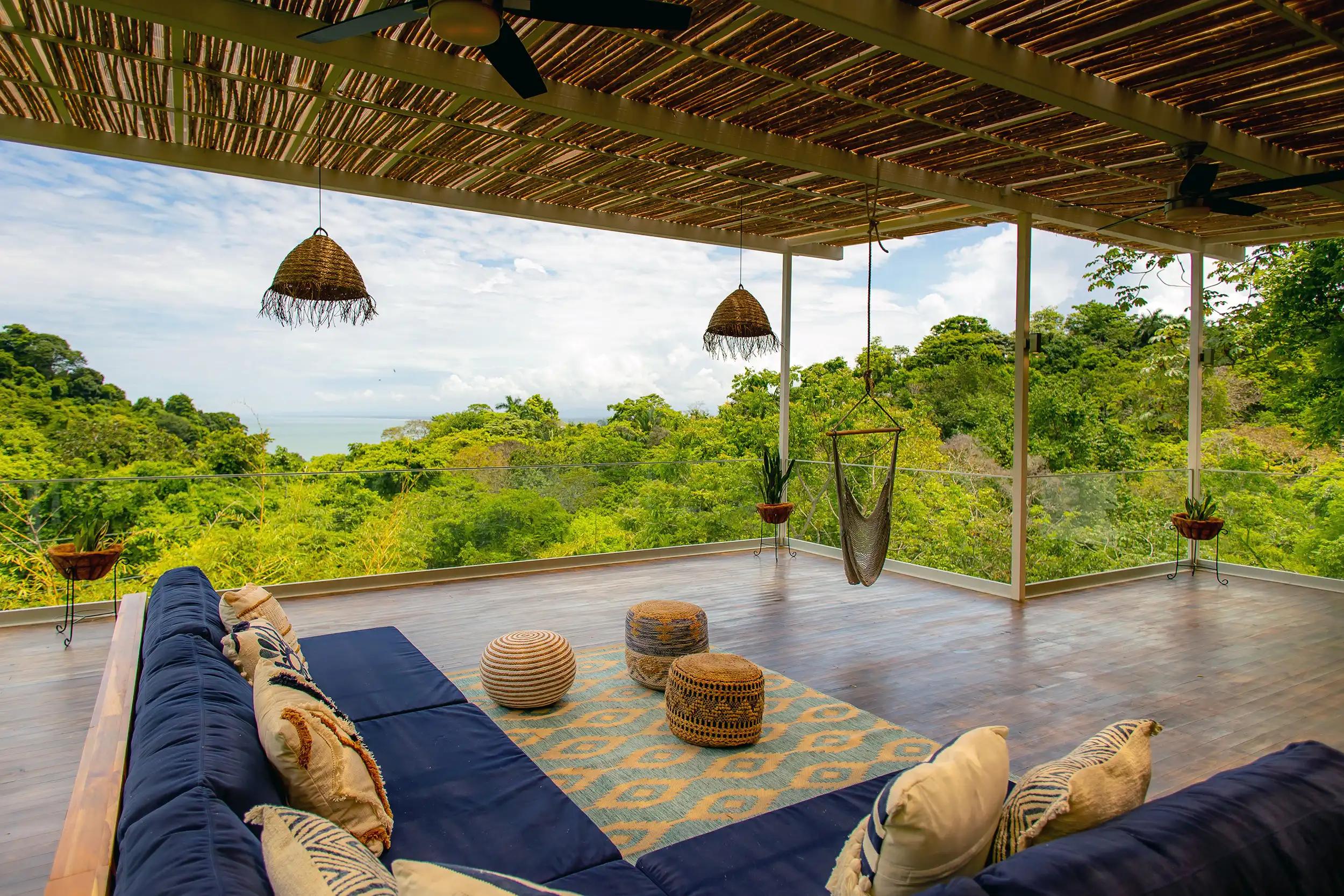 Villa Caimito's terrace lounge with poufs, hammock chair, and sweeping jungle and sea views