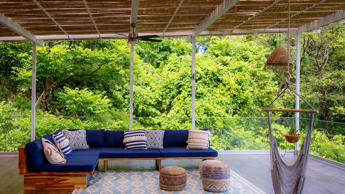 Sofa with striped pillows and a hammock chair overlooking the treetops at Villa Caimito