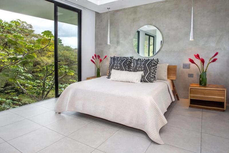 Bedroom at Casa Nueva Vida with round mirror, concrete wall, and treetop window view