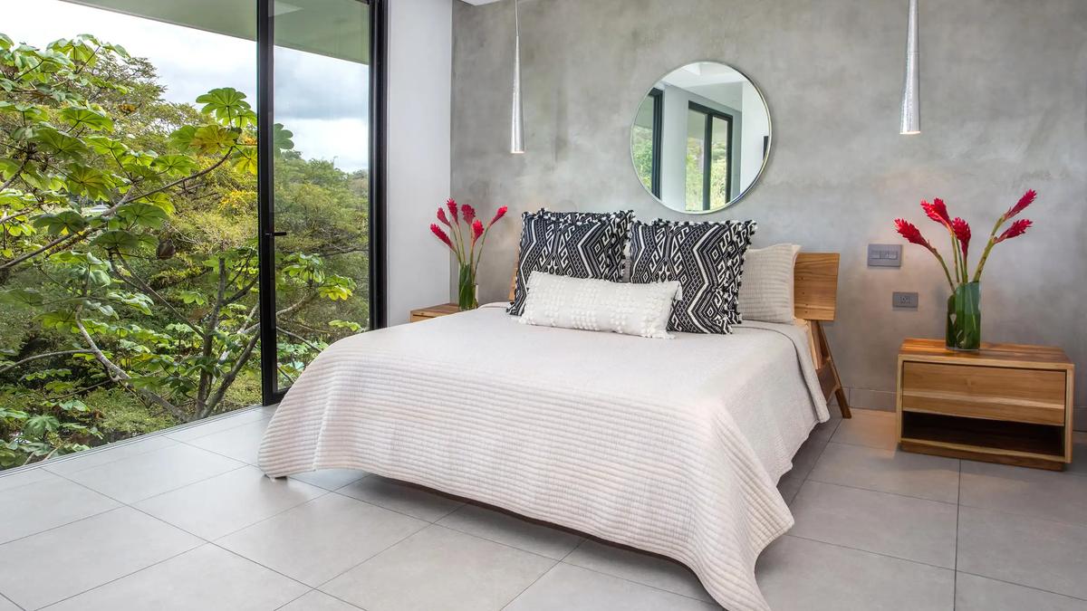 Bedroom at Casa Nueva Vida with round mirror, concrete wall, and treetop window view