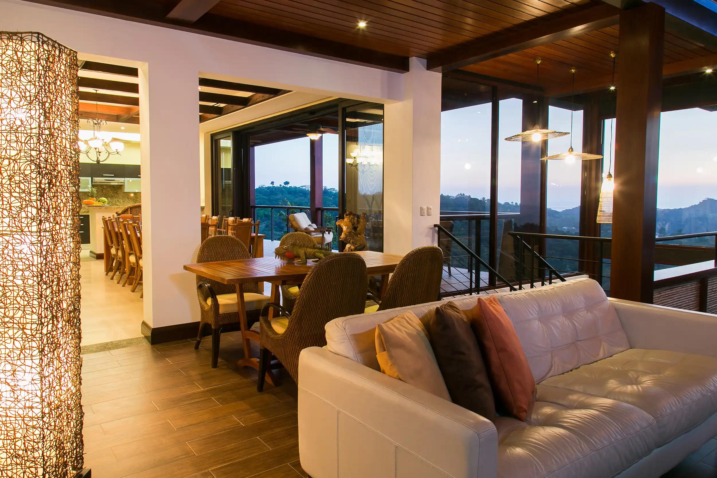 Leather sofa and wicker dining chairs at Villa Celaje looking out over dusk-lit hills