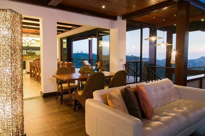 Leather sofa and wicker dining chairs at Villa Celaje looking out over dusk-lit hills