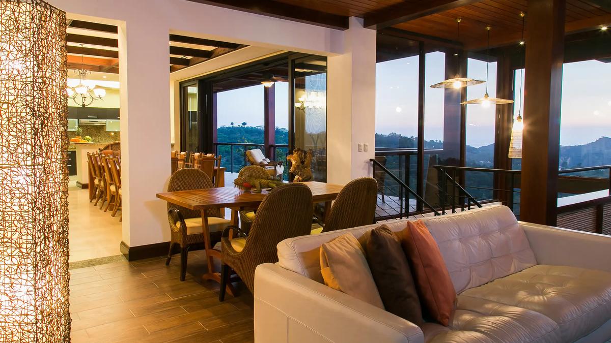 Leather sofa and wicker dining chairs at Villa Celaje looking out over dusk-lit hills