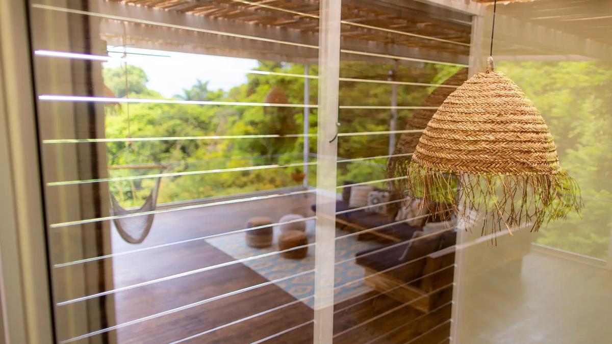 Woven pendant lamp beside glass walls reflecting Villa Caimito's treetop terrace