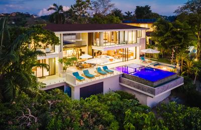 Casa Nola glowing at dusk with lit infinity pool, terrace, and jungle surroundings