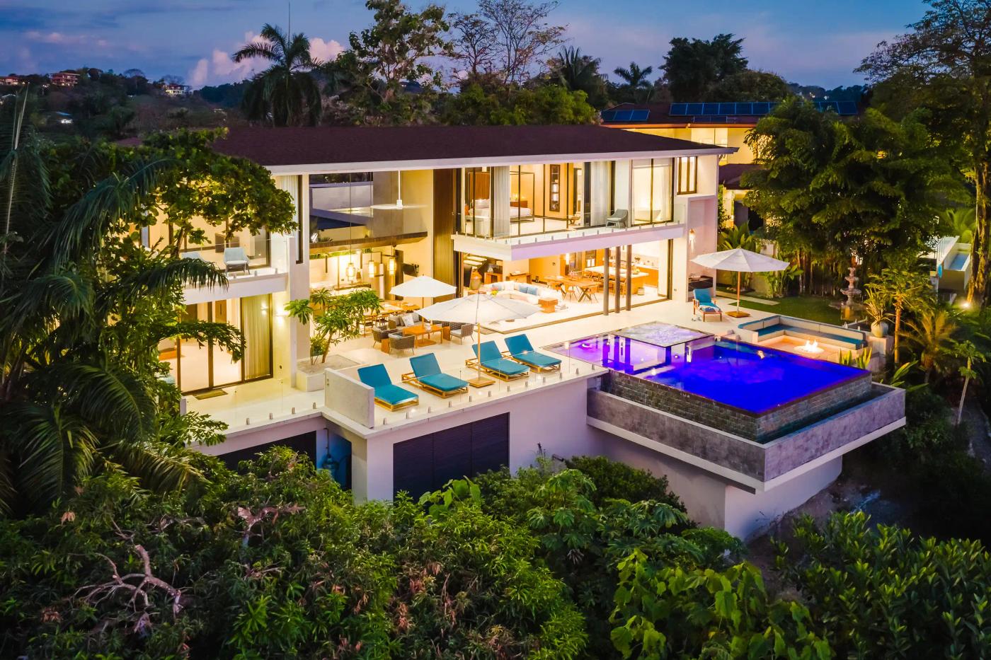 Casa Nola glowing at dusk with lit infinity pool, terrace, and jungle surroundings