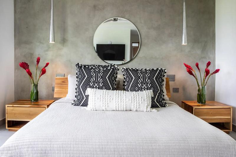 Bed at Casa Nueva Vida with patterned pillows, teak nightstands, and red ginger flowers