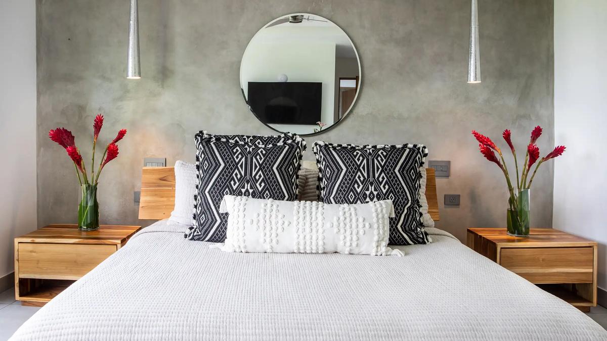 Bed at Casa Nueva Vida with patterned pillows, teak nightstands, and red ginger flowers