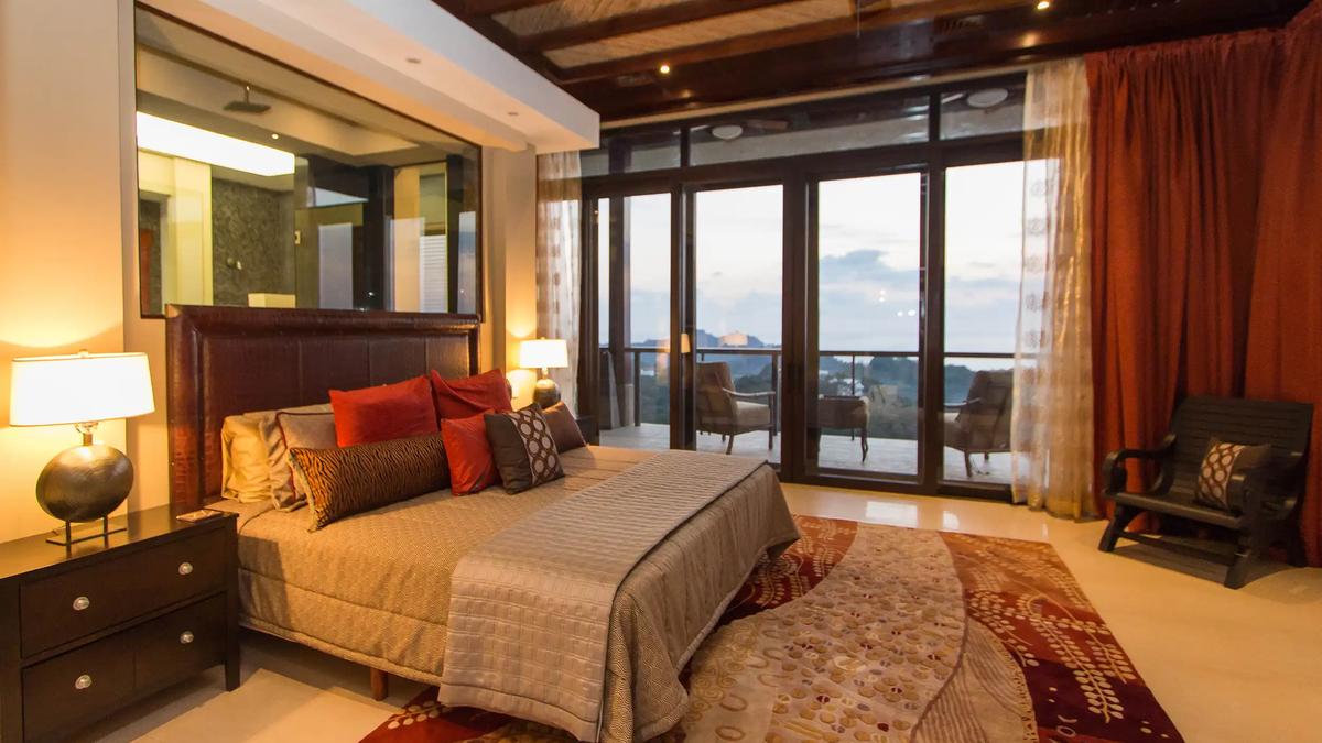 Master bedroom at Villa Celaje with red accent pillows and terrace doors to an ocean sunset