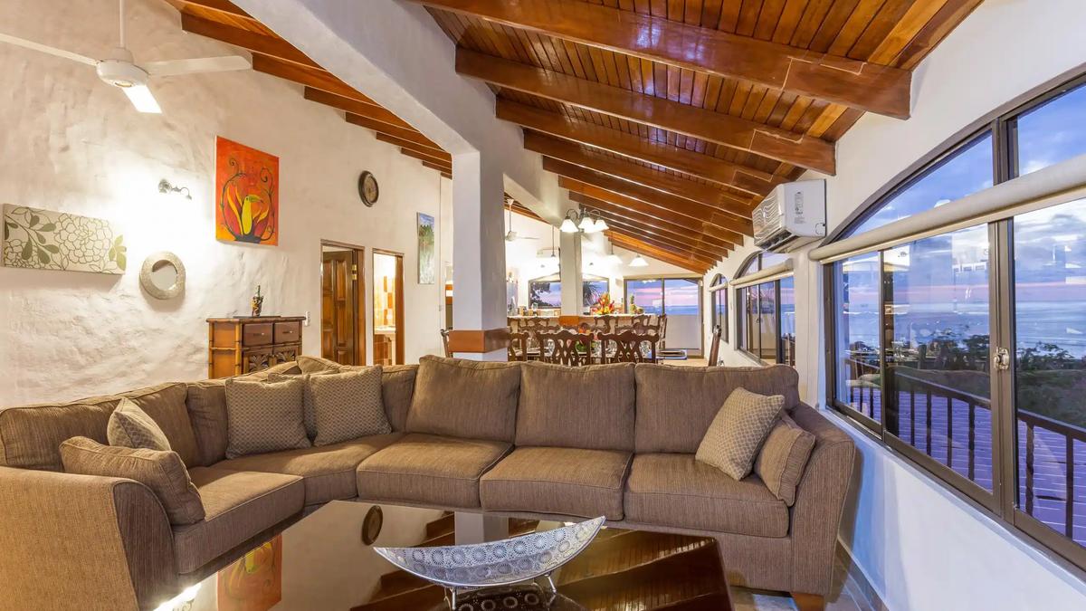 Large sectional sofa at Casa Moreno beneath wood beams with sunset ocean windows