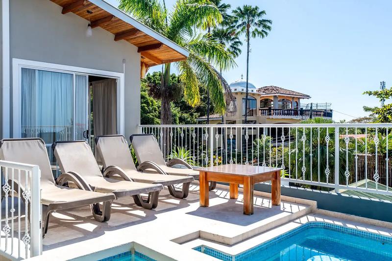 Four sun loungers and a wooden table on the pool deck at Casa Alta Vista