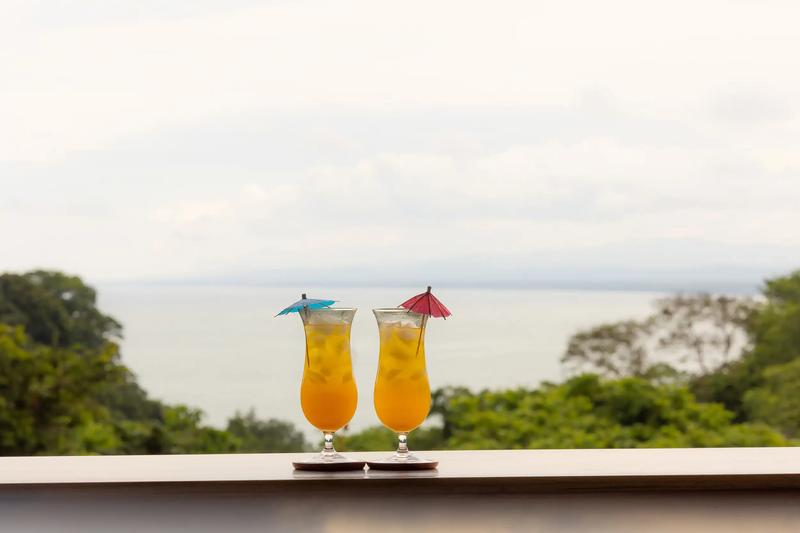 Two tropical drinks with paper umbrellas on a Villa Caimito railing overlooking the sea