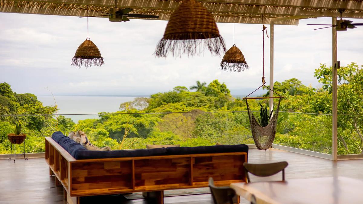 Wicker pendant lights above Villa Caimito's lounge, with the Pacific visible past the rainforest
