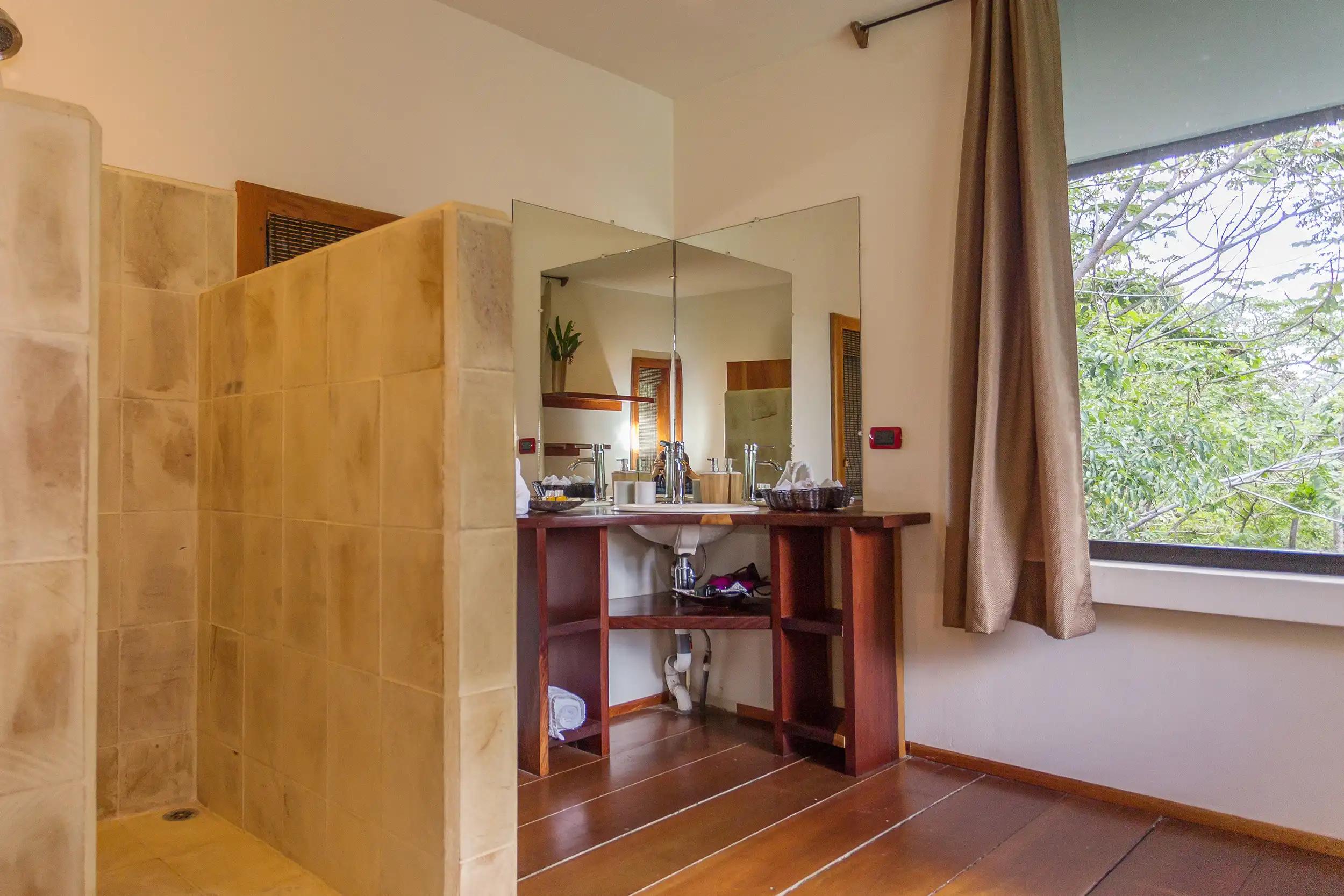 Stone tiled walk-in shower and corner wood vanity in a Casa Luz bathroom