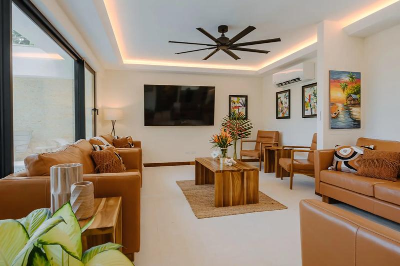 Living room at Casa Rambutan with caramel leather sofas, ceiling fan, and tropical paintings
