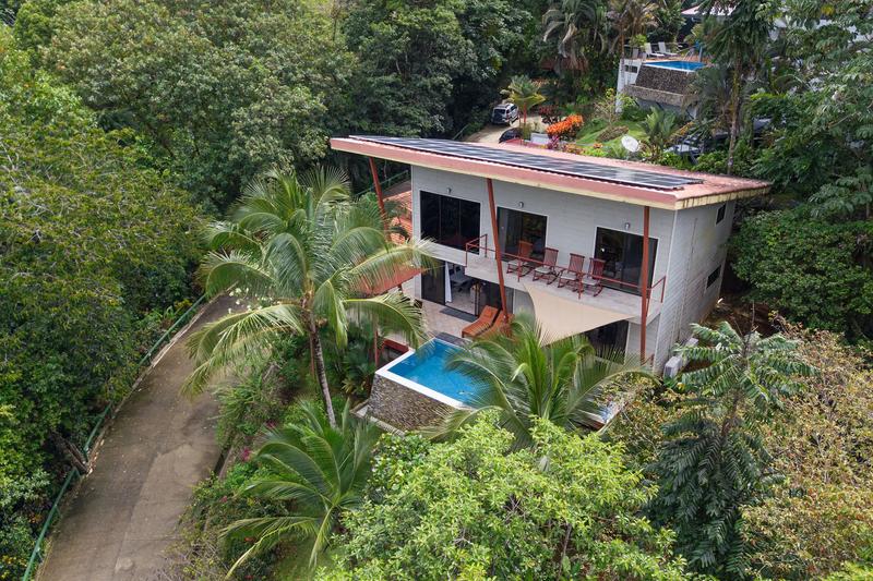 Casa Serenidad's white facade and pool surrounded by rainforest palms, seen by drone