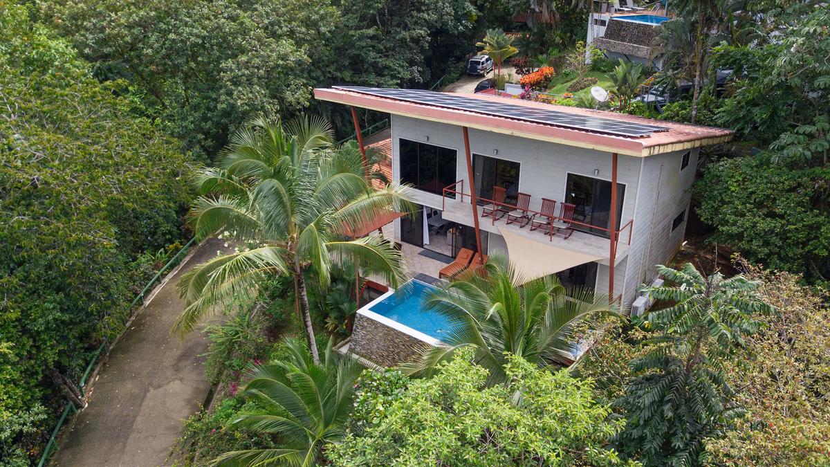 Casa Serenidad's white facade and pool surrounded by rainforest palms, seen by drone