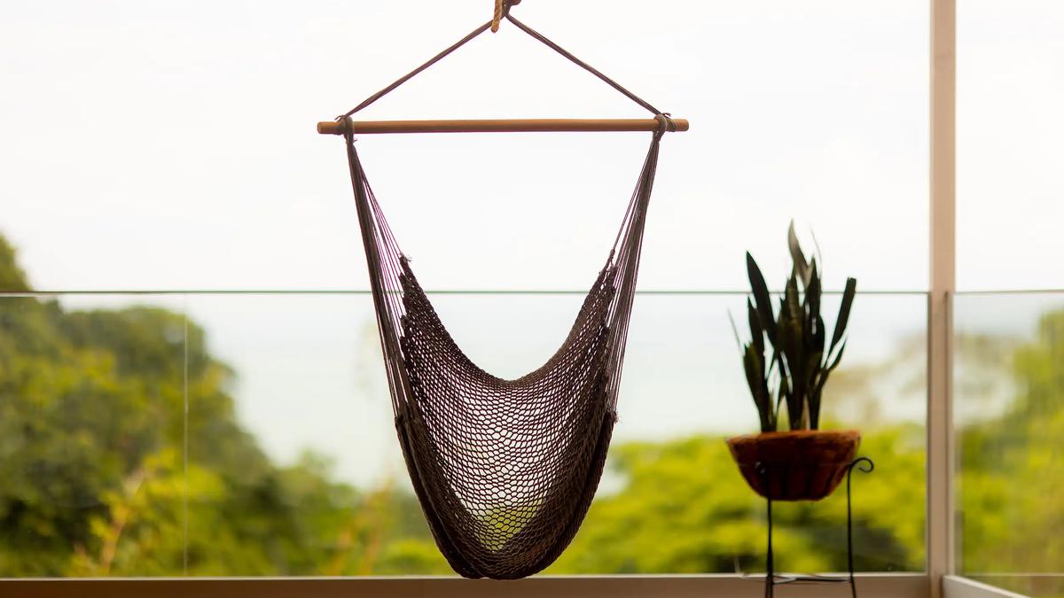 Rope hammock chair hanging by the glass railing at Villa Caimito with jungle beyond