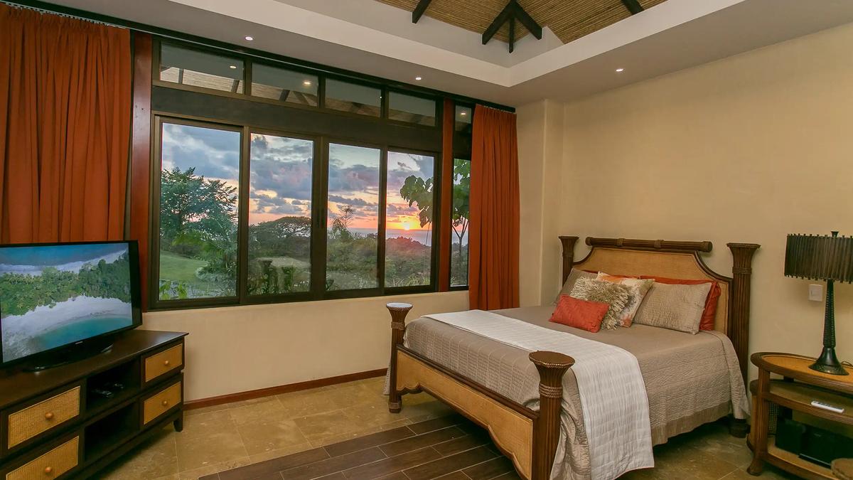 Queen bedroom with sunset ocean views through wide windows at Casa Anaka