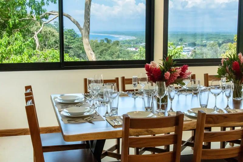 Dining table at Casa Rambutan set for dinner beside windows with coastline views