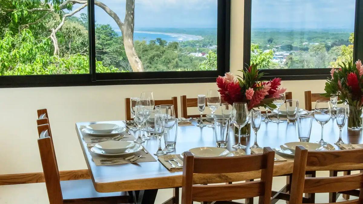 Dining table at Casa Rambutan set for dinner beside windows with coastline views