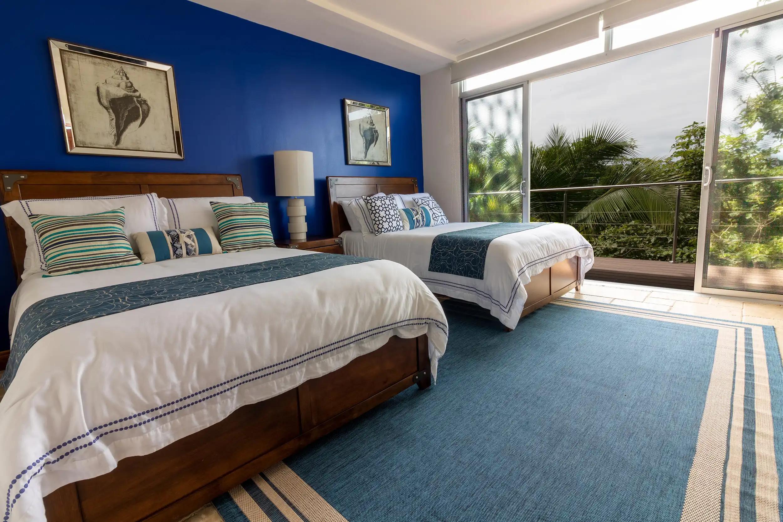 Two queen beds with blue accent wall and jungle views at Casa Contee