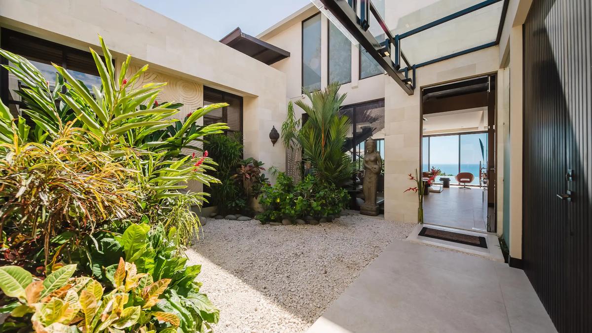 Entry courtyard at Casa Nola with tropical plants, stone statue, and ocean glimpse beyond