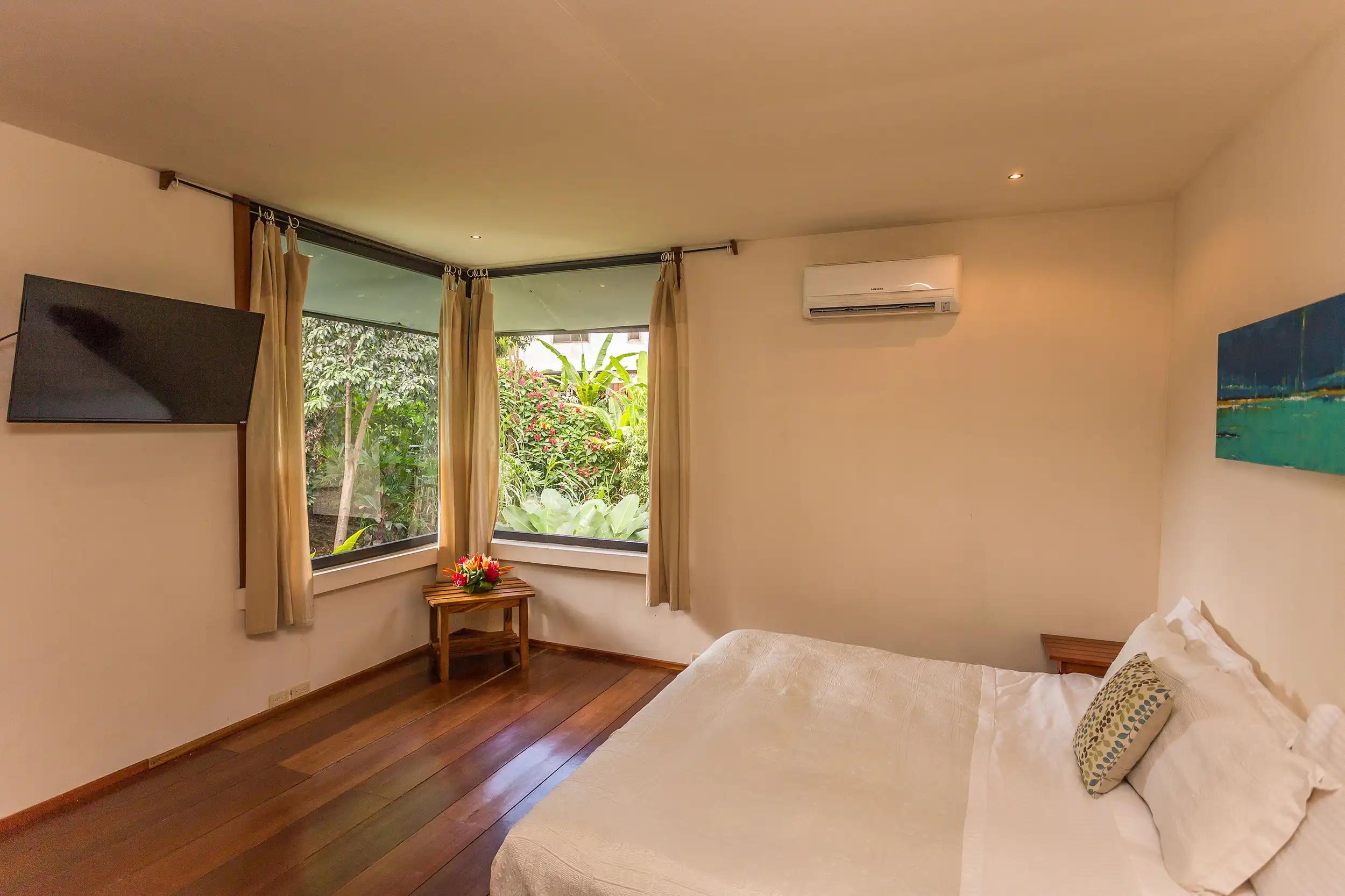 Casa Luz bedroom with corner garden windows, wood floor and mounted TV