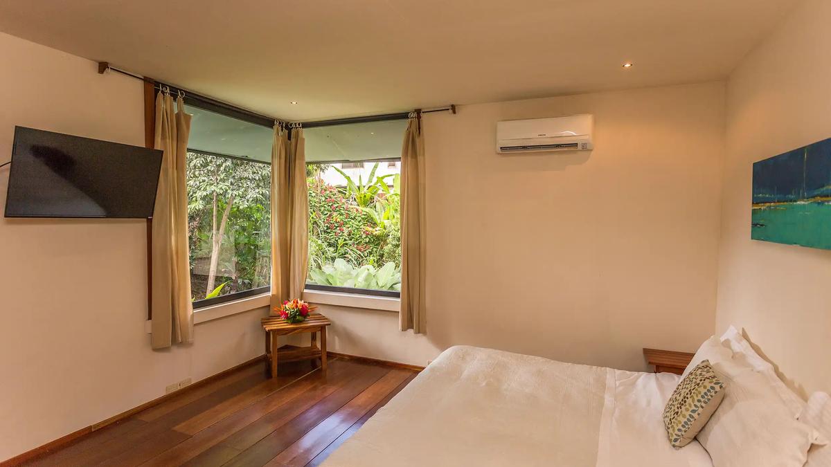 Casa Luz bedroom with corner garden windows, wood floor and mounted TV