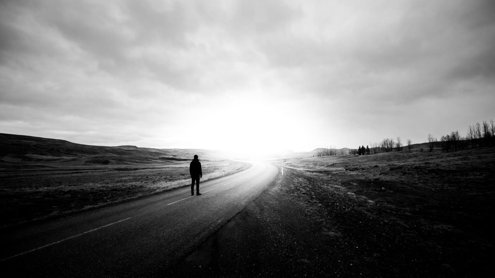 A lone figure on an open road heading toward bright light