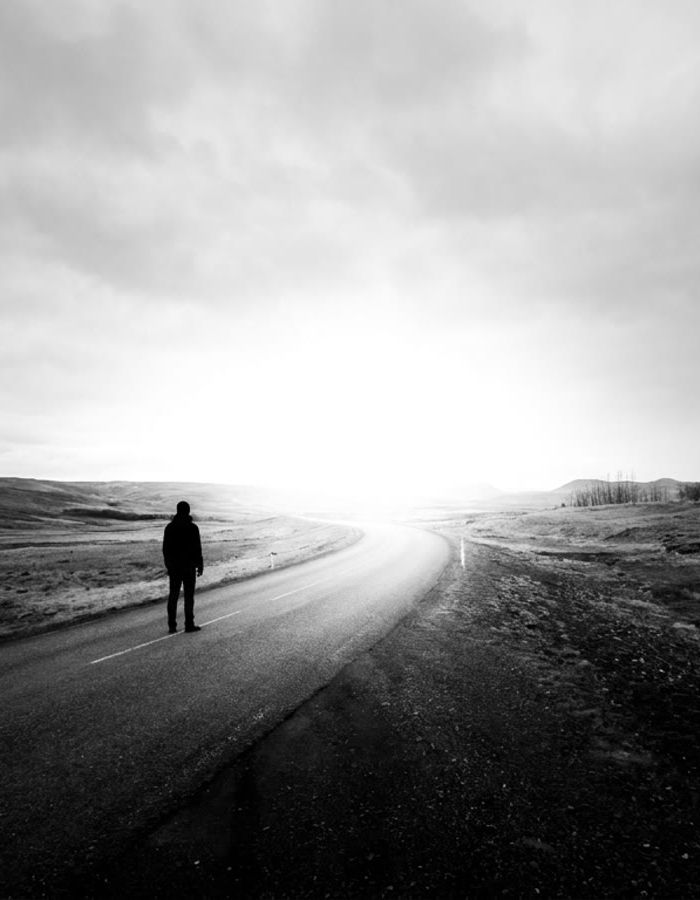 A lone figure on an open road heading toward bright light
