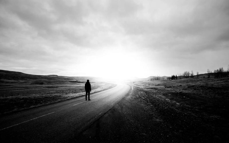 A lone figure on an open road heading toward bright light