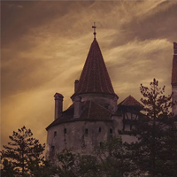 A historic castle with conical towers set against a dramatic, cloudy sky, partially obscured by surrounding trees.
