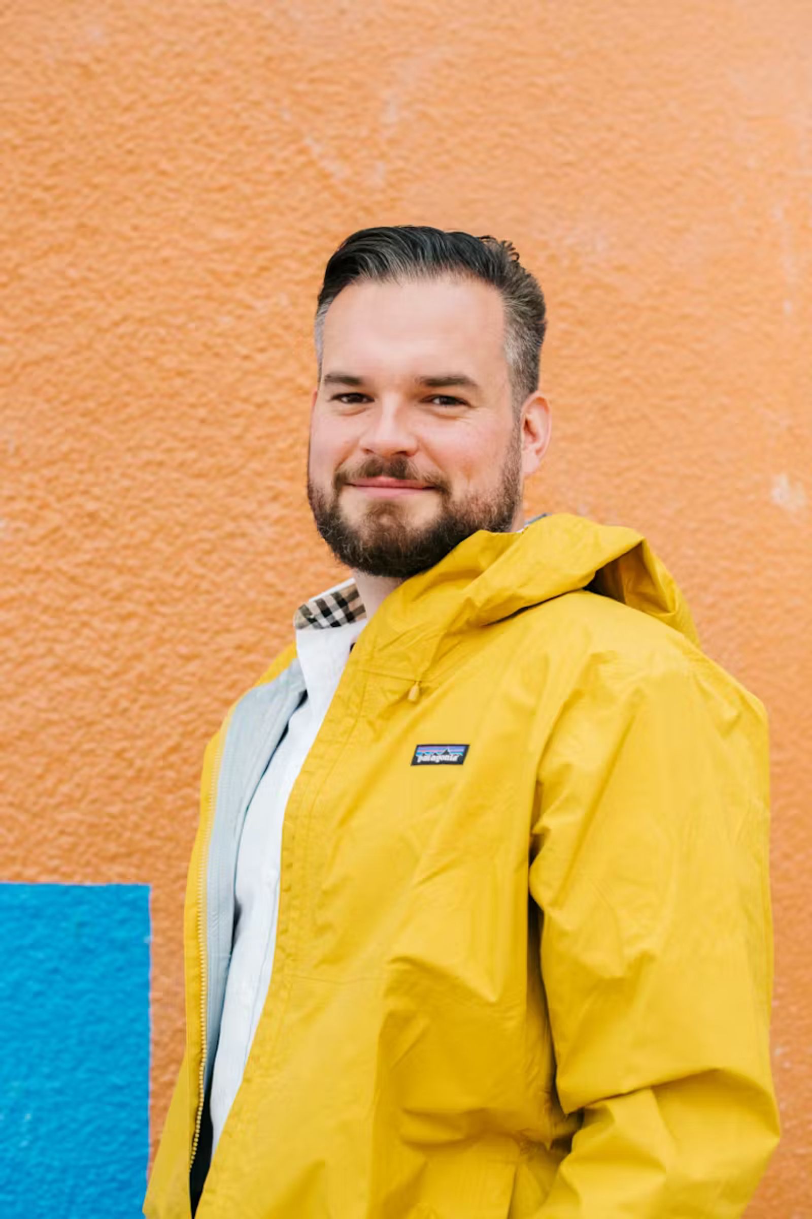 A man wearing a yellow jacket smiling in front of an orange wall