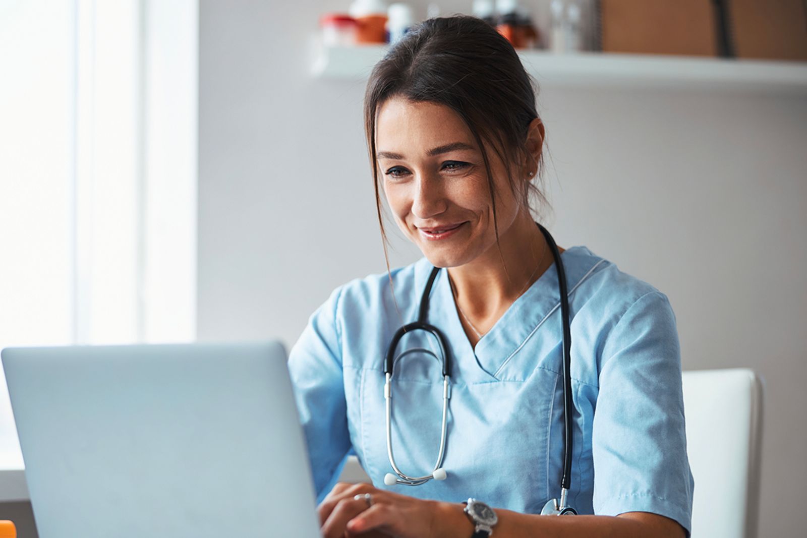 Female healthcare professional in scrubs using a laptop during a virtual consultation