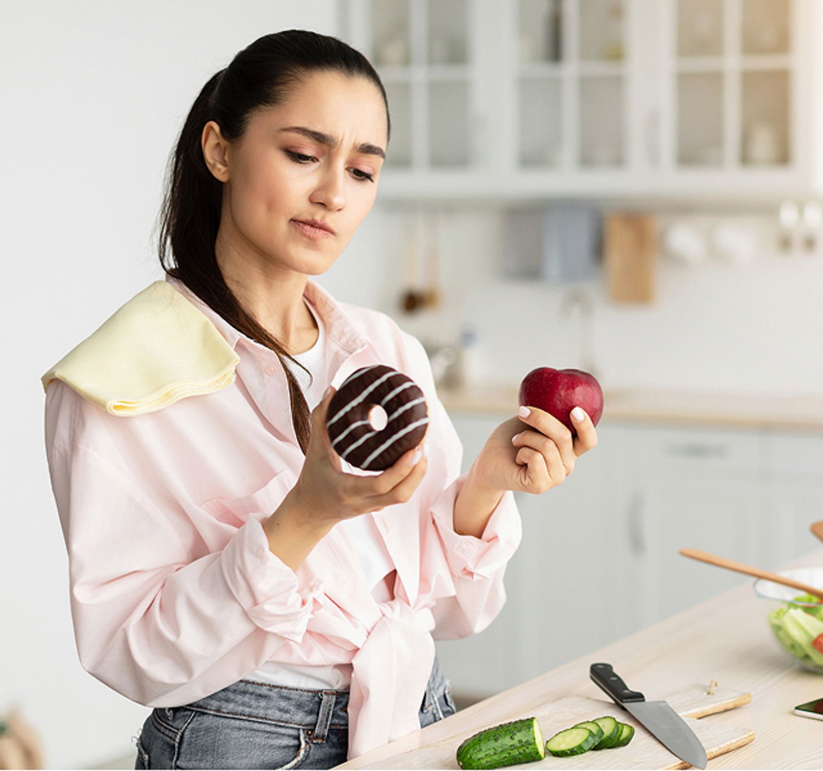 Woman comparing a donut and an apple while preparing food in a kitchen
