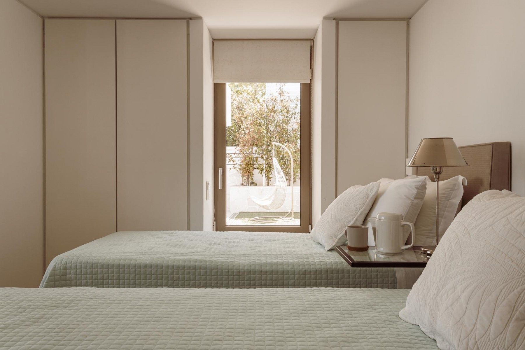 Spacious twin-bedroom with soft neutral tones and morning sunlight.