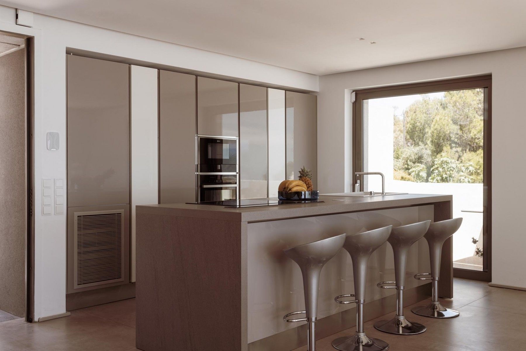 A modern kitchen with a sleek island, bar stools, and panoramic views at SeaClusion Luxury Villa.