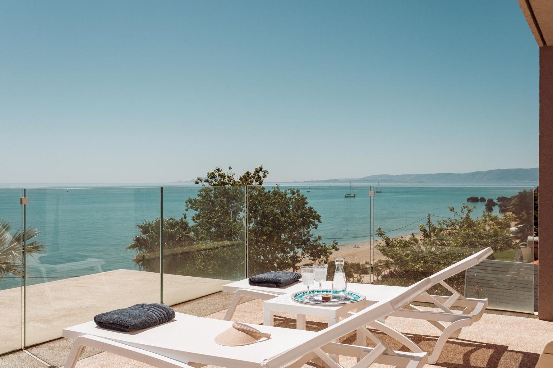 A sunlit pool area with lounge chairs and a view of the Ionian Sea.