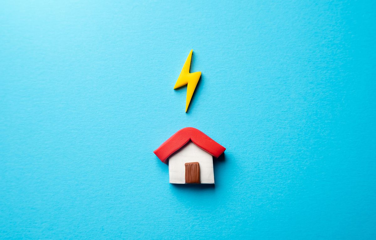 Clay model house with a yellow lightning bolt above it on a bright blue background
