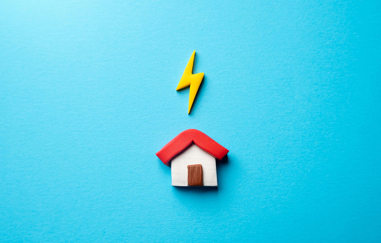 Clay model house with a yellow lightning bolt above it on a bright blue background