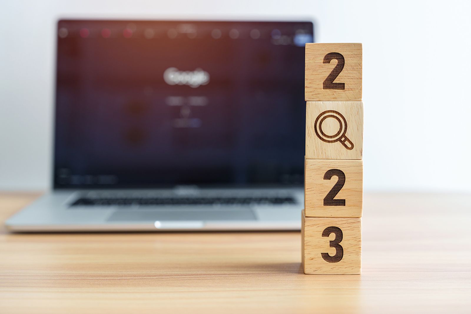Wooden blocks stacked to read 2023 with a magnifier icon in front of a laptop