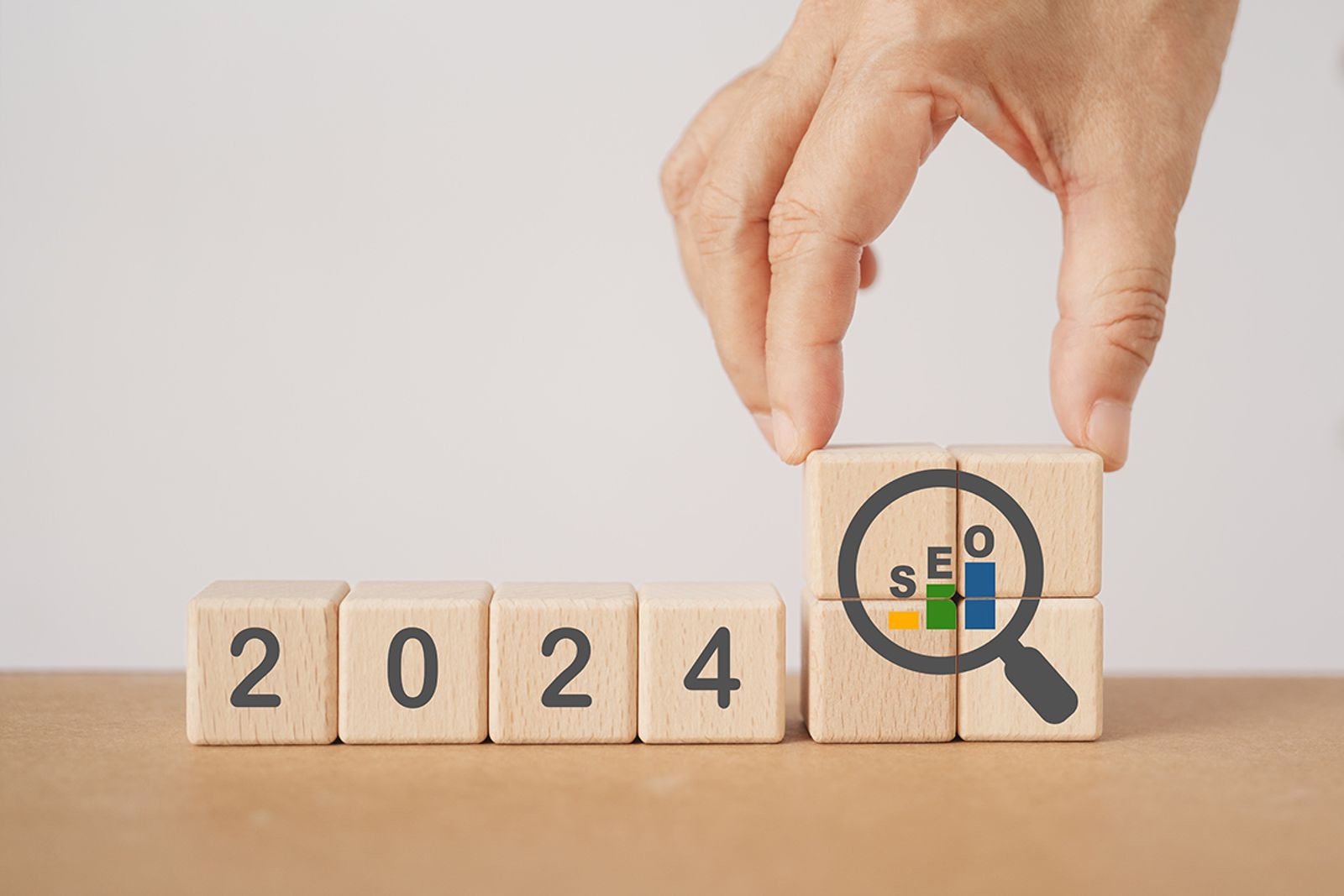 Hand turning wooden blocks reading 2024 next to a magnifying glass SEO icon