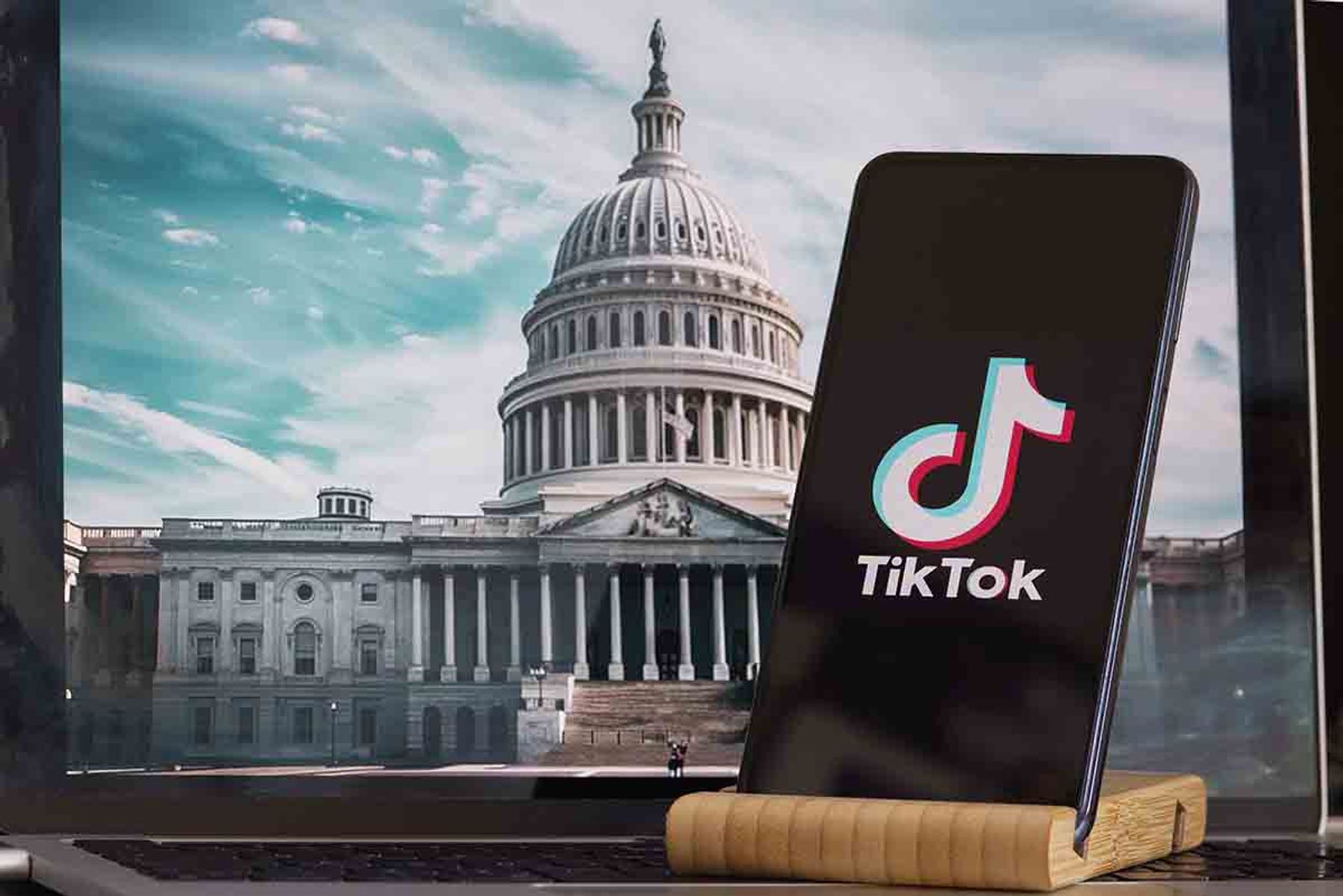 Smartphone displaying the TikTok logo propped in front of a screen showing the U.S. Capitol