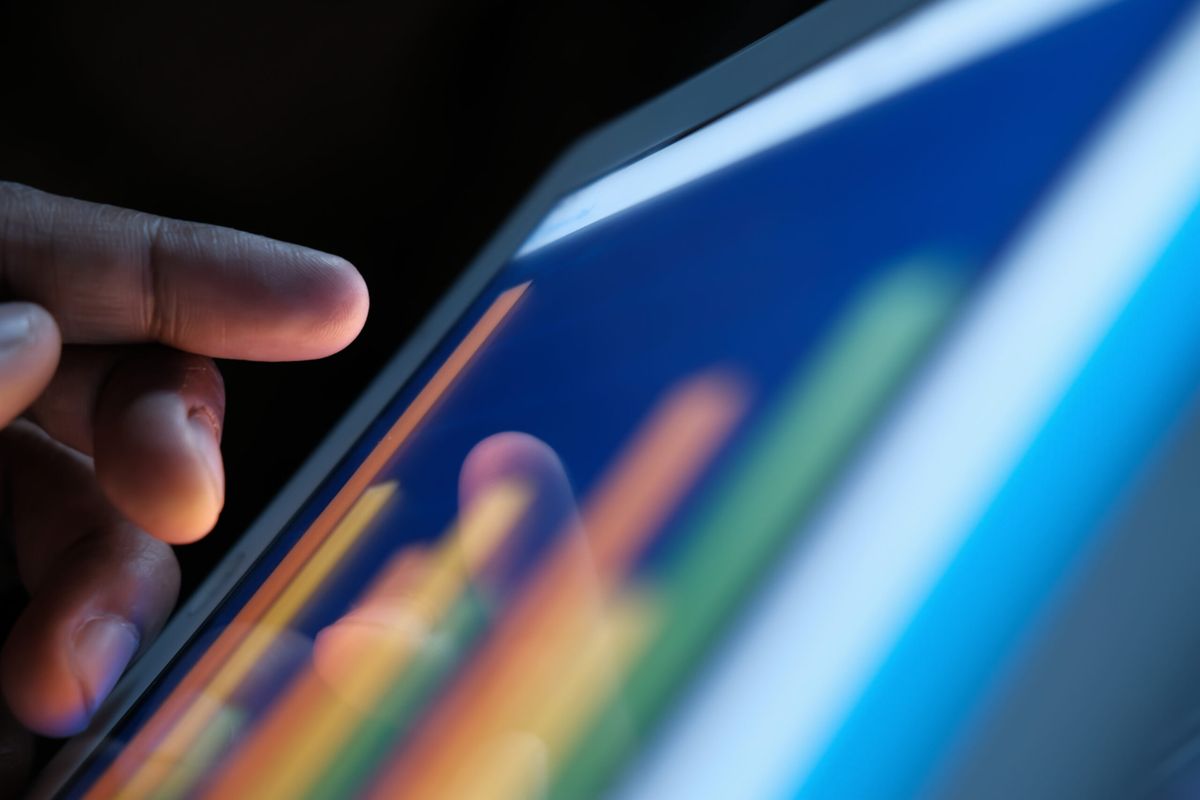 Finger touching a tablet screen showing glowing colorful performance bars in a dark room
