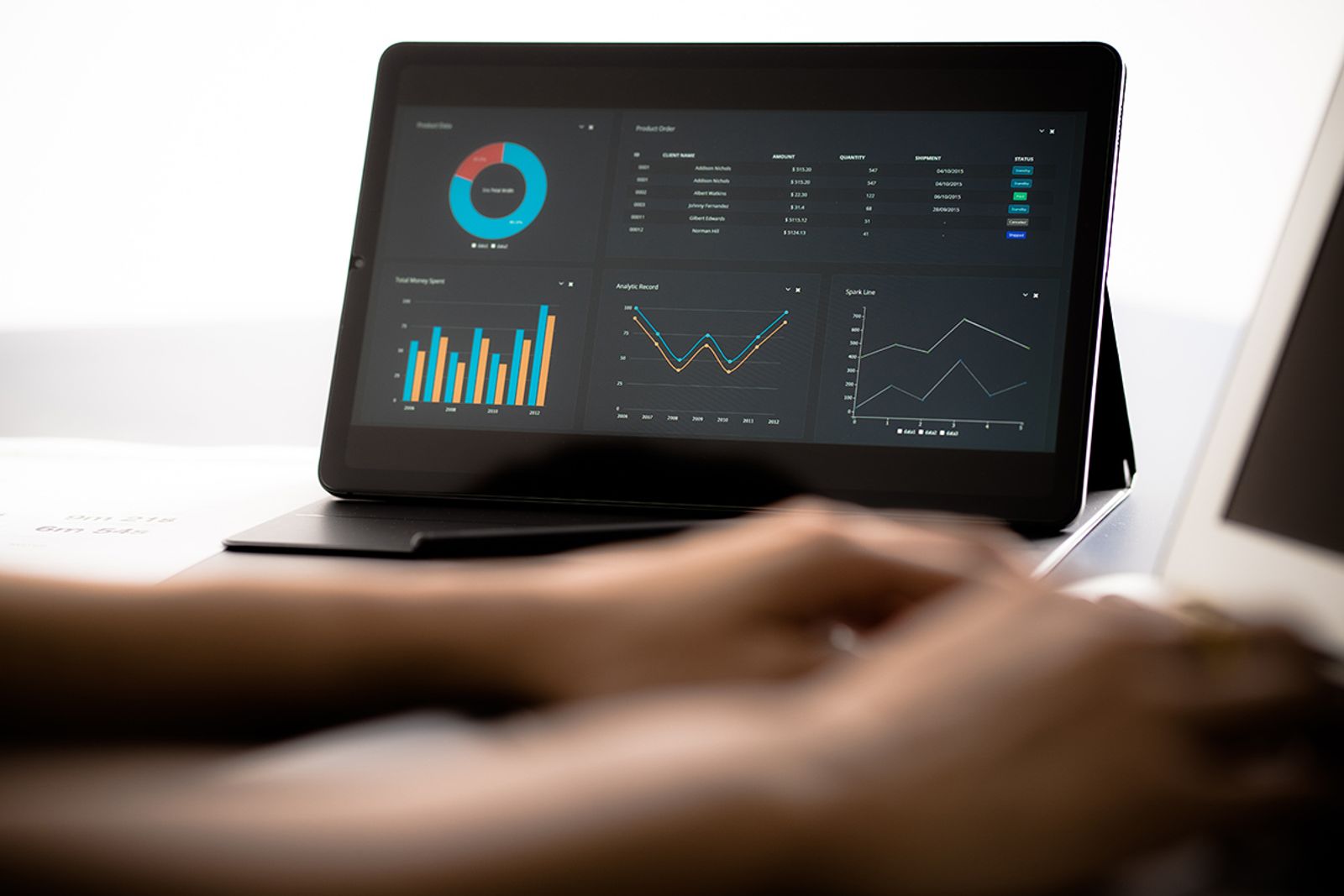 Hands typing at a tablet showing a dark analytics dashboard with charts and campaign data