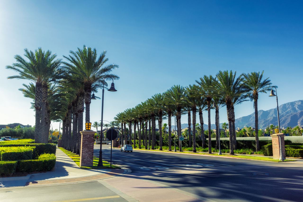 A palm-lined boulevard in Ontario, California, with the San Gabriel Mountains in the distance.